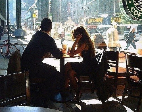 Молодой парень в кафе пьет кофе и смотрит на красивую девушку за соседним столиком.